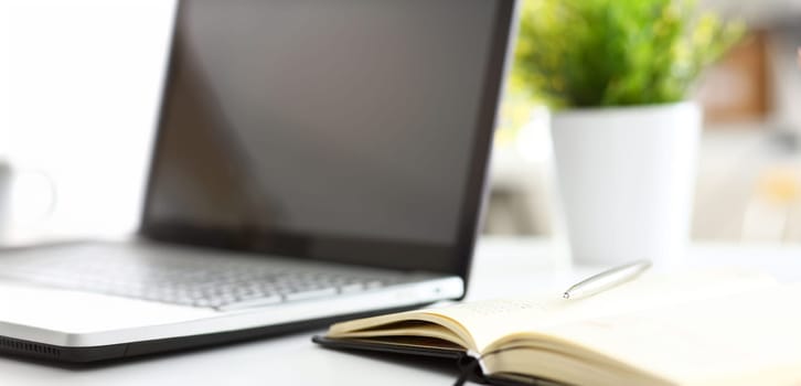 Silver pen lying on opened notebook sheet closeup in office with laptop pc on worktable. Inspector occupation for student examination or career strategy personal training course signature concept
