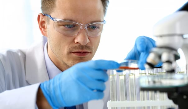 Male chemist holds test tube of glass in hand portrait overflows liquid solution potassium permanganate conducts an analysis reaction takes various versions of reagents using chemical manufacturing.