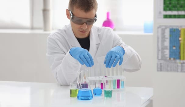 A male chemist holds test tube of glass in his hand overflows a liquid solution of potassium permanganate conducts an analysis reaction takes various versions of reagents using chemical manufacturing.