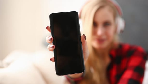 Portrait woman at home in headphones sitting on the couch holding a smartphone in hands remote education studying of foreign languages alone