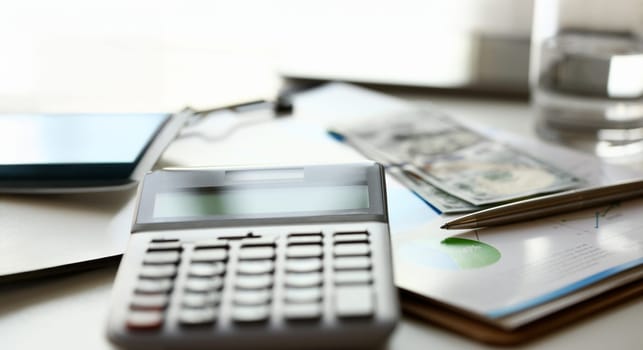 Silver calculator with gray keyboard is lying on desk graph and pen office setting. Calculation of family expenses social income population freelance irs situation growth research concept
