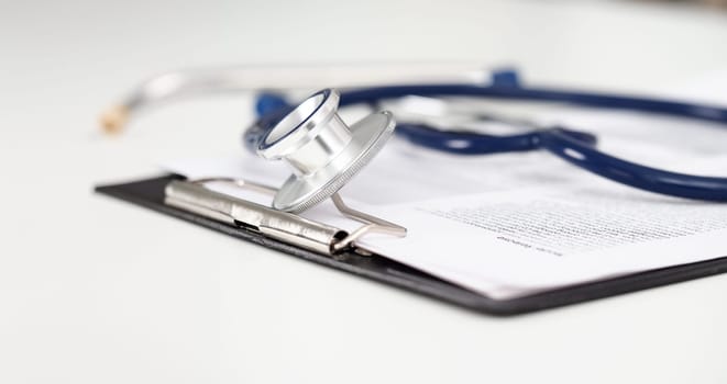 Stethoscope head lying on medical form on clipboard pad at empty doctor worktable. Physical disease prevention examine patient 911 instrument shop healthy lifestyle concept