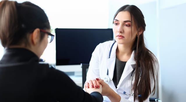 Young female doctor holds sick patient by hand expressing condolences and sympathy reports bad news about loss of loved ones due to cancer deadly aids disease and says we can handle support concept.