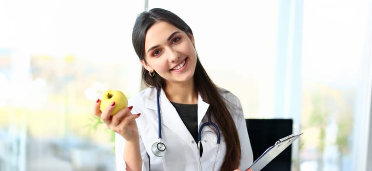 Young smiling woman doctor holds apple in hand portrait. Nutritionist talks about concept of healthy diet lifestyle for losing excess weight about benefits and harms vegetarianism.