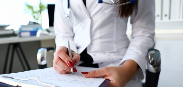 Female doctor hand hold silver pen filling patient history list at clipboard pad. Physical exam er disease prevention ward round visit check 911 prescribe remedy healthy lifestyle concept