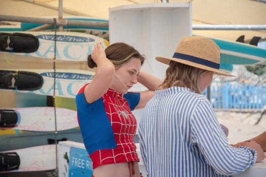 Teenage girl in swimsuit with Spiderman print and her mother choose water activities from the manager rental of water sports equipment, entertainment on the beach, Belek, Turkey, May 30, 2024
