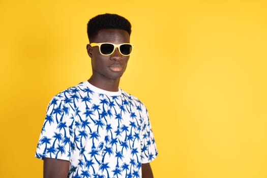 A man wearing a blue and white shirt with palm trees on it stands in front of a yellow background