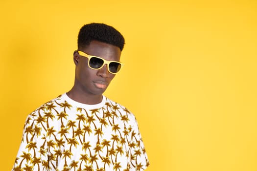 A man wearing sunglasses and a yellow shirt with palm trees on it. He is standing in front of a yellow wall
