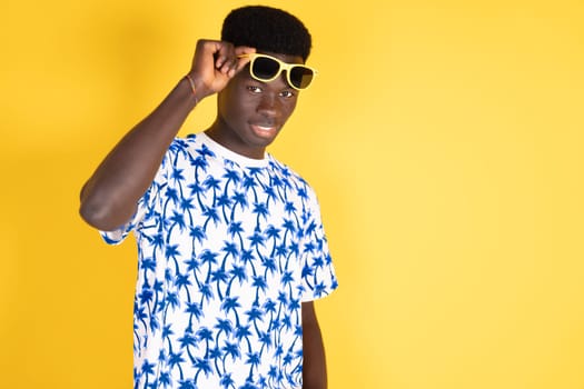 A man wearing a blue and white shirt with palm trees on it is posing for a picture. He is wearing sunglasses and has a smile on his face. The image has a bright and cheerful mood