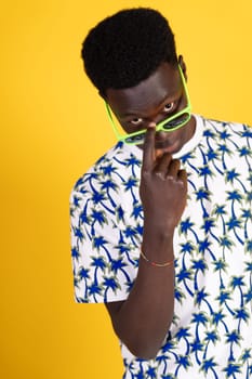 A man with glasses and a green shirt with palm trees on it. He is looking at the camera and has his nose pressed to his face