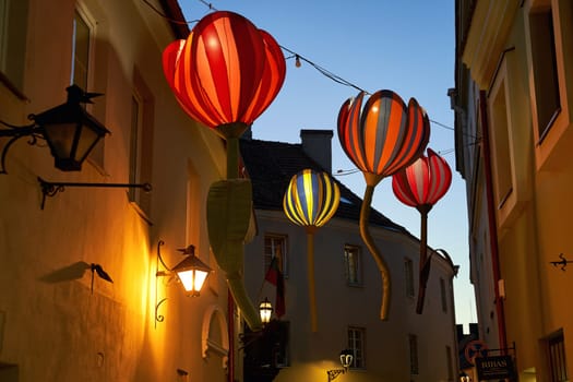 Vilnius, Lithuania - May 27, 2024: Huge artificial flowers hanging over the old street at dusk