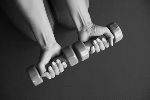 Woman hands holding pink dumbbells on green sport mat background. Home exercise during pandemic.