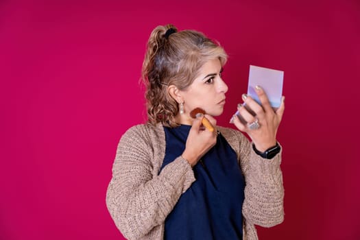 Pretty young woman putting on makeup on a red background, Copy space. Beauty concept.