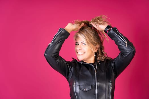 A woman with long hair is wearing a black leather jacket and smiling. The jacket is zipped up and has a collar