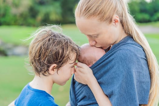 Mom walks with a newborn in a sling and also with her teenage son. This scene showcases the bond within the family, highlighting the nurturing care of a mother and the connection between siblings.
