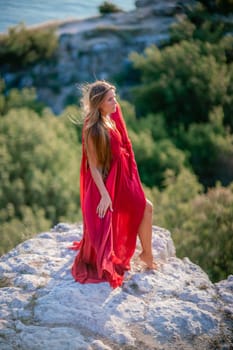 Woman sunset sea red dress, back view a happy beautiful sensual woman in a red long dress posing on a rock high above the sea on sunset