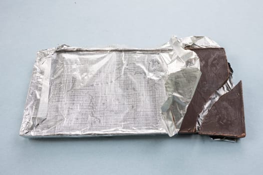 Opened chocolate with unpacked foil, cracked chocolate, broken piece of chocolate bar.