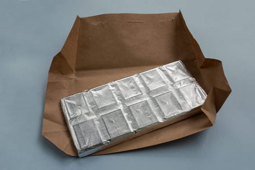 Chocolate in foil with opened paper packaging.New chocolate in craft paper.