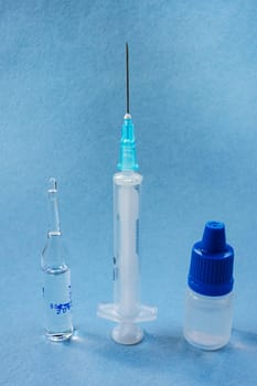 Two different syringes for injections and a plastic bottle with medicine on a blue background.