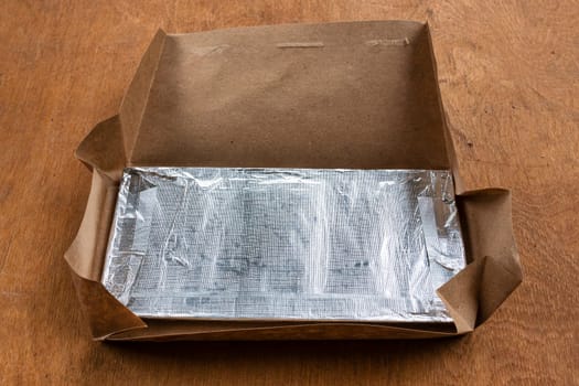 Chocolate in foil with opened brown paper packaging on a wooden background.