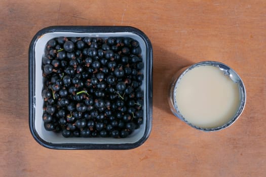 Opened can of condensed milk, black currant berry in metalware on brown wooden background, top view. The concept of healthy eating.