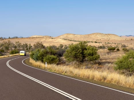 A yellow caravan travels along a winding road through the picturesque Flinders Ranges, South Australia.