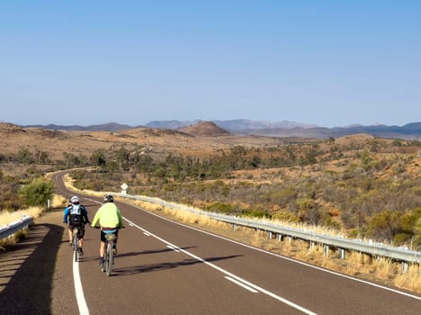 A cyclist rides along a scenic road in the Flinders Ranges, South Australia, with mountains in the distance.