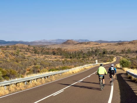 A cyclist rides along a scenic road with mountains in the distance.