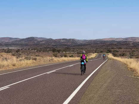 A cyclist rides along a scenic road with mountains in the distance.