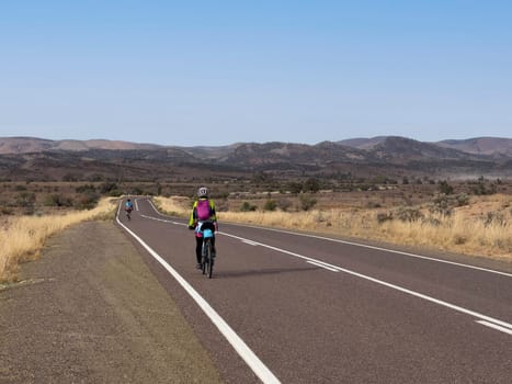 A cyclist rides along a scenic road in the Flinders Ranges, South Australia, with mountains in the distance.