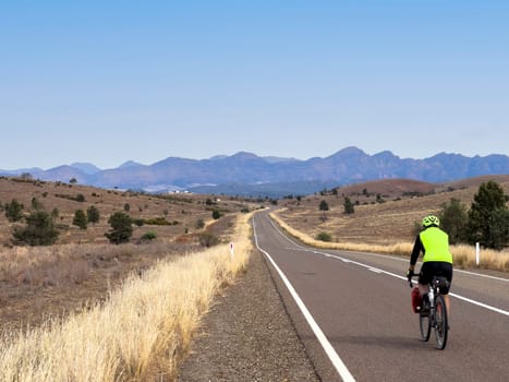 A cyclist rides along a scenic road in the Flinders Ranges, South Australia, with mountains in the distance.