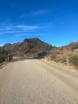 A winding dirt road leads through rugged Ikara Flinders Ranges under a clear blue sky.