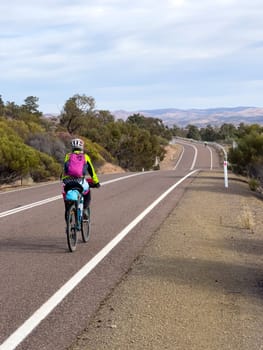 A cyclist rides along a scenic road with mountains in the distance.