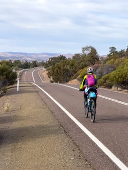 A cyclist rides along a scenic road in the Flinders Ranges, South Australia, with mountains in the distance.