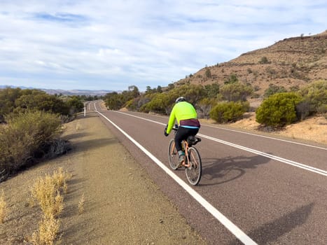 A cyclist rides along a scenic road in the Flinders Ranges, South Australia, with mountains in the distance.