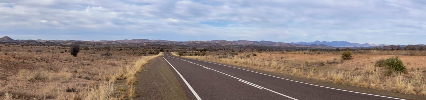 A wide, empty road stretches through the expansive, rugged terrain of the Flinders Ranges, South Australia.