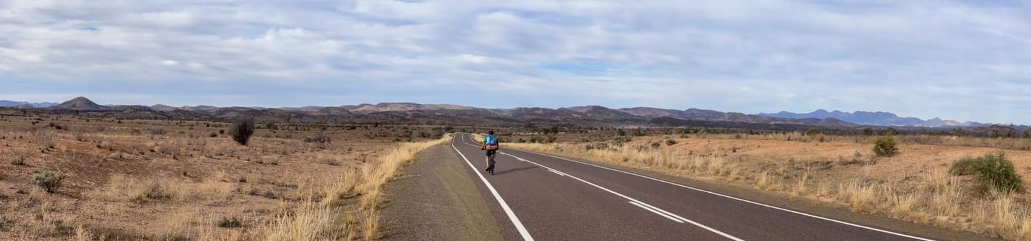 A lone cyclist rides along a vast, scenic road in the Flinders Ranges, South Australia.