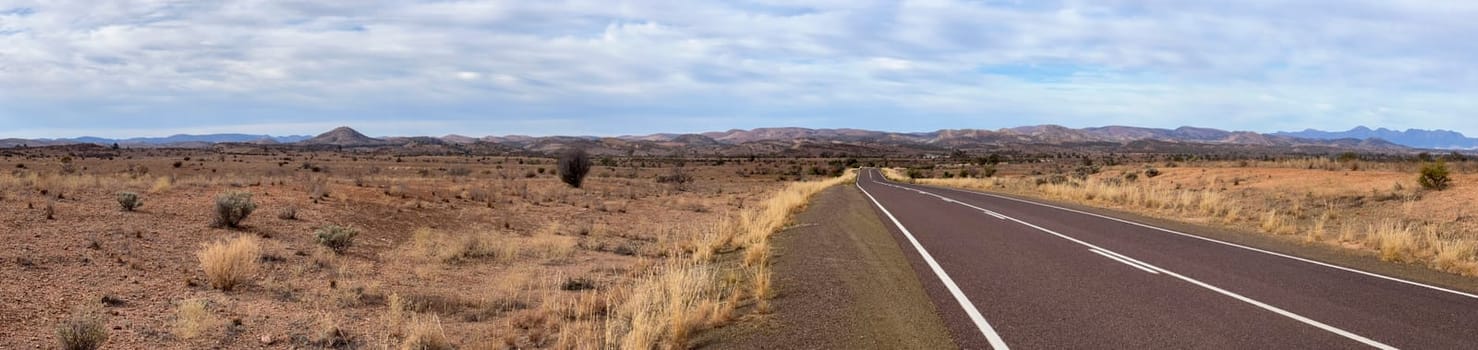 A wide, empty road stretches through the expansive, rugged terrain of the Flinders Ranges, South Australia.