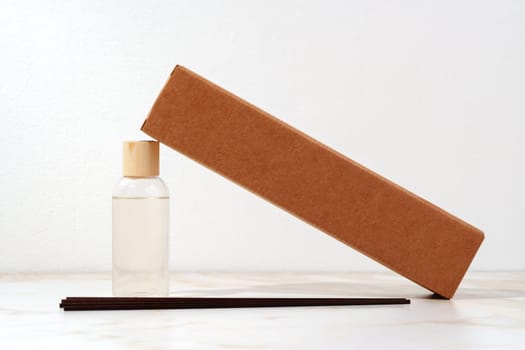 A brown cardboard box is lying on its side with one end propped up against a glass bottle that has a wooden cap.