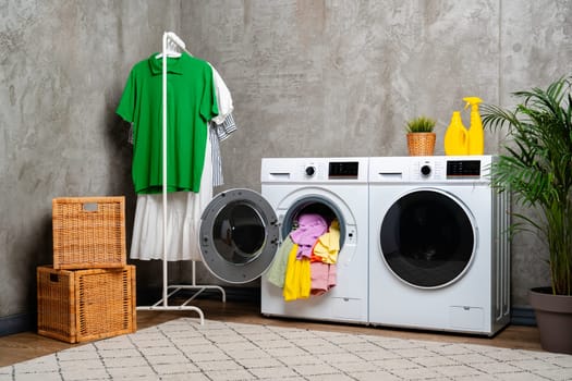 A white front-loading washing machine with the door open, revealing a pile of colorful clothes inside.