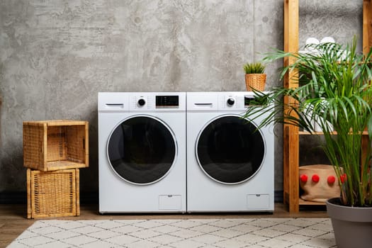 A modern laundry room with two white washing machines, a plant in a pot, and wicker baskets.