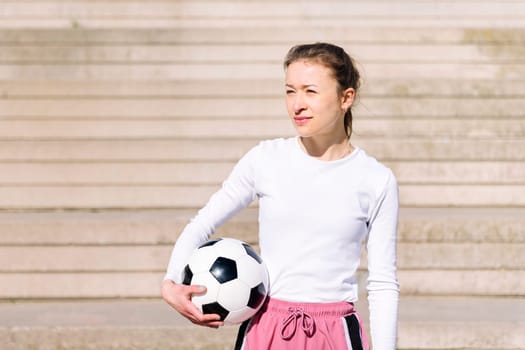 sports woman in a concrete soccer court with a ball under her arm, concept of football lifestyle and urban sport in the city, copy space for text