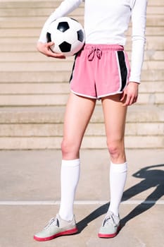 close up of an unrecognizable sports woman in a concrete soccer court with a ball under her arm, concept of football lifestyle and urban sport in the city
