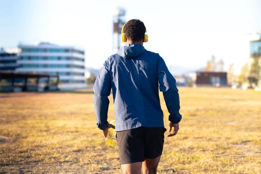Young runner wearing headphones holding cold isotonic sports water in his hand