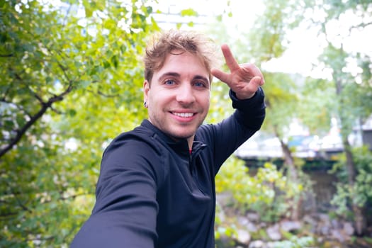 Cheerful young man taking a selfie showing peace sign with a cell phone