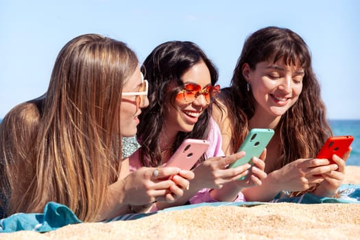 Group of smiling multiethnic women enjoying vacation. Beautiful and cheerful Gen Z girls with their mobile phones pose looking at the camera with a mobile phone.