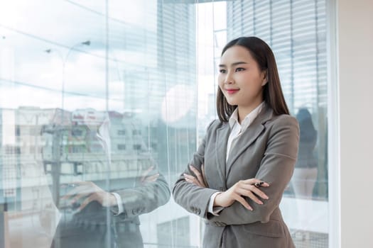 Confident young accountant in professional attire, standing with arms crossed in a modern office, looking out the window.