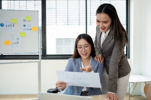 Two female accountants work together on financial graphs in a modern office, showcasing teamwork and professional collaboration.