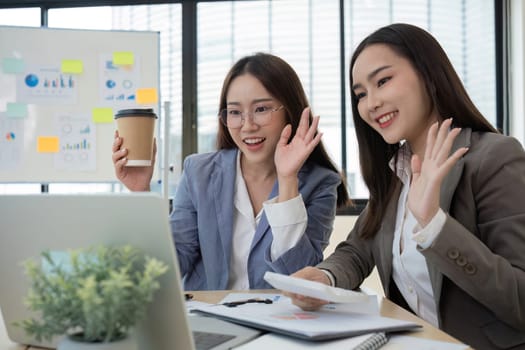 Two female accountants work together on financial graphs in a modern office, using laptops and enjoying coffee.