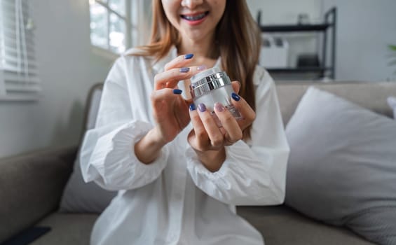 A young woman enjoys her morning skincare routine, applying face cream in a modern home environment, emphasizing self-care and beauty.